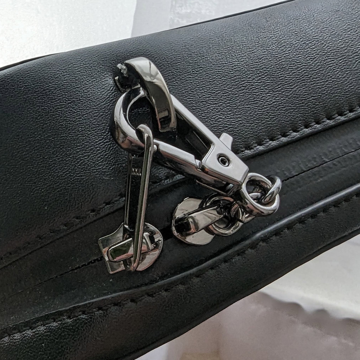 Anti-theft Water-resistant Travel Crossbody - Elise Crossbody in Black Gunmetal with slash-resistant faux leather & locking clasps straps - closeup of zipper clasp to strap attachment - Arden Cove